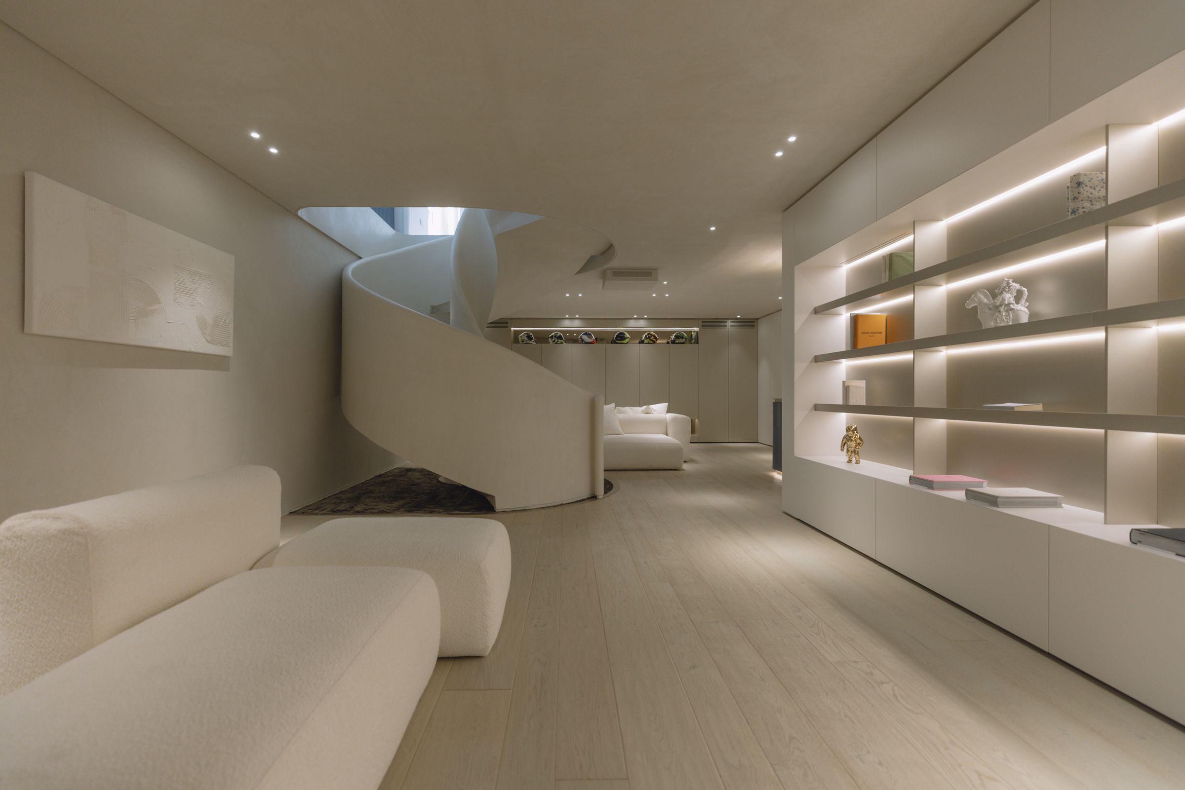 Lower floor with the helical staircase and a long fitted wall with lit shelves