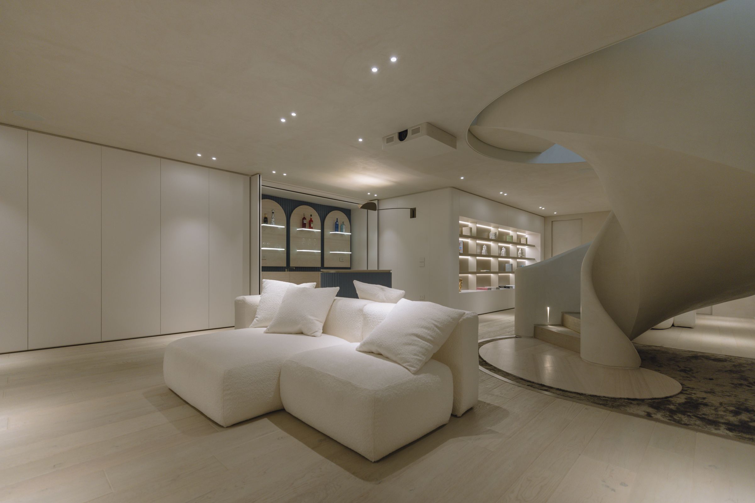 Lounge area with a white sofa, a blue bar cabinet with lit niches and the helical staircase