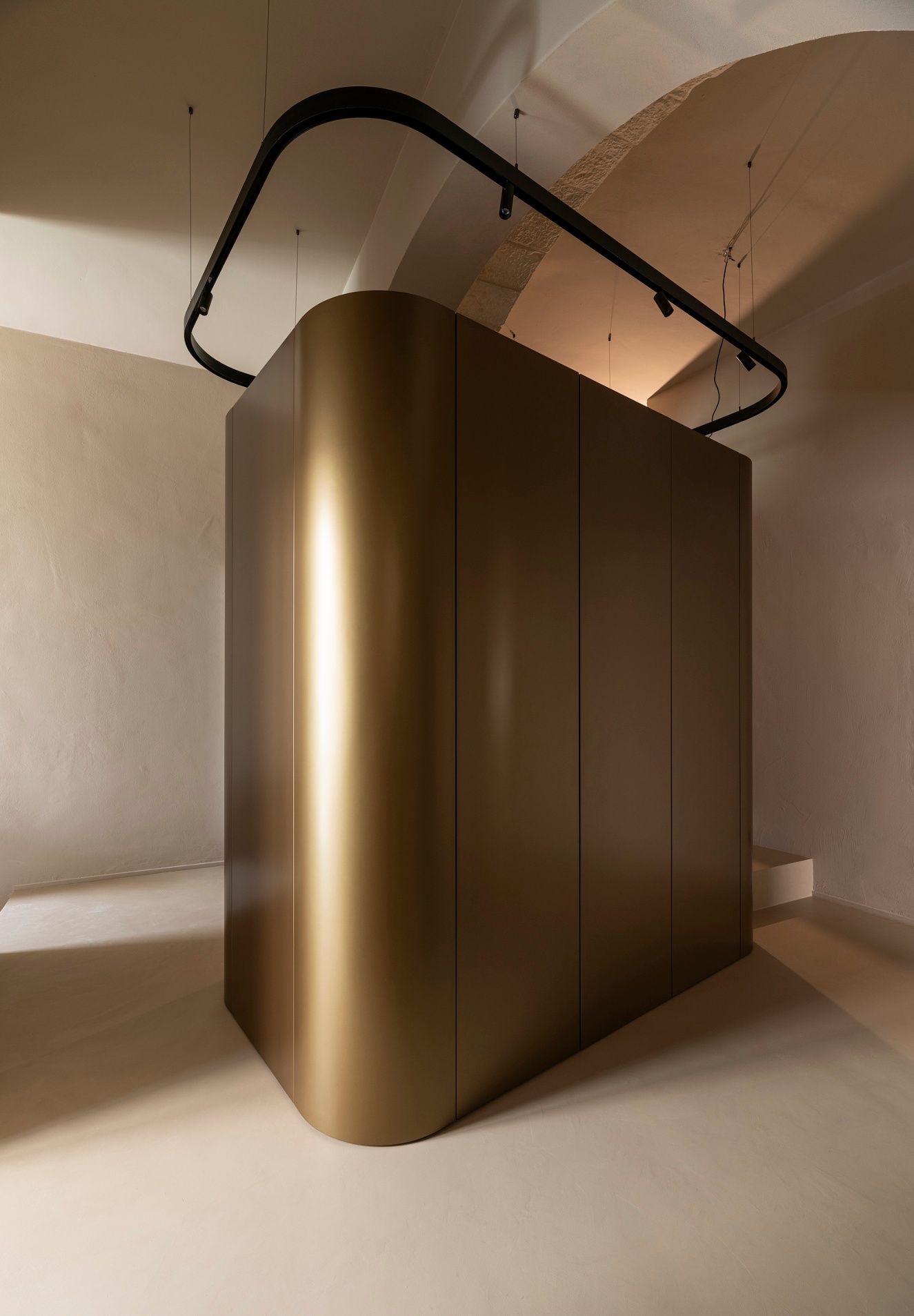 Curved bronze-finish metal volume beneath a stone vault